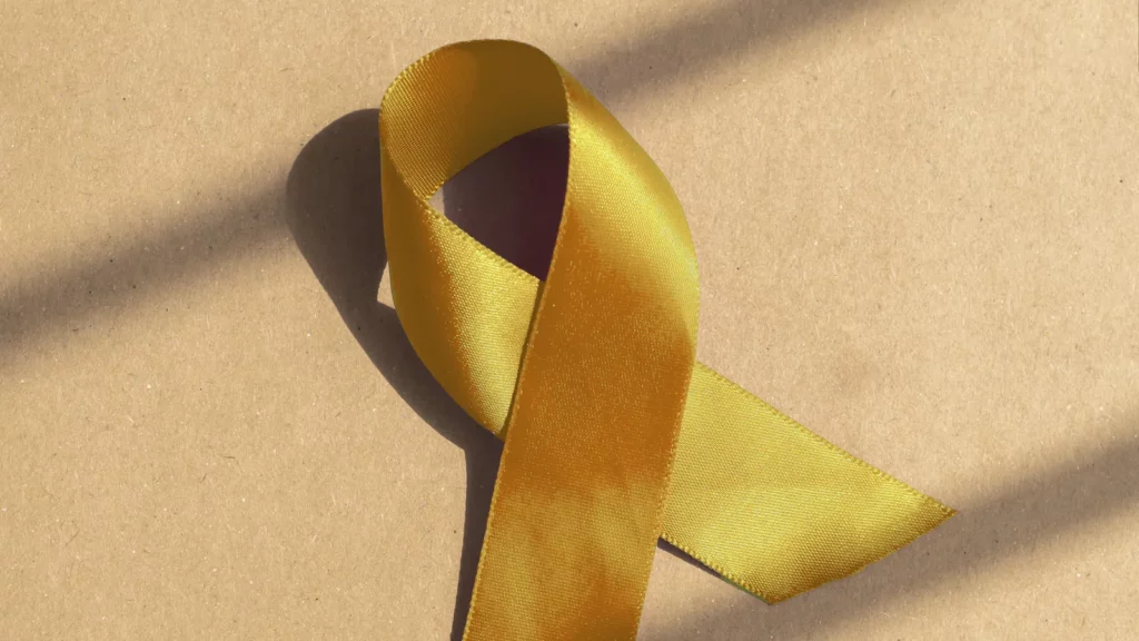 Ruban doré en satin, symbole des cancers de l'enfant, posé sur un fond kraft clair traversé par des rais de lumière