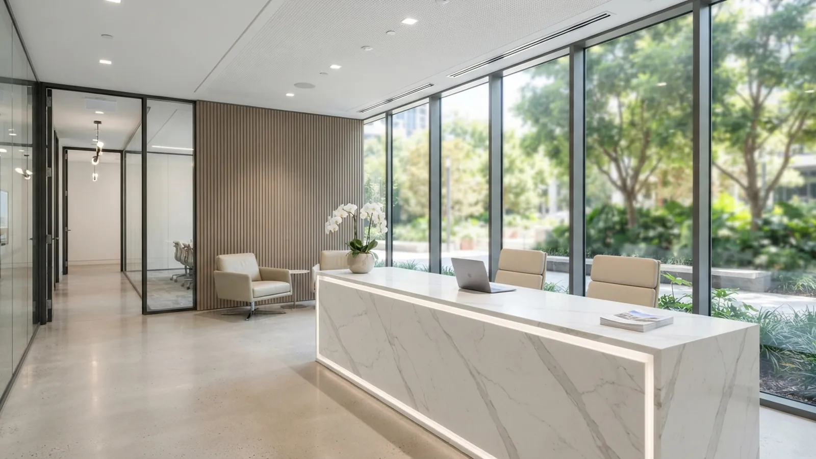 Hall d'accueil lumineux avec comptoir en marbre clair, fauteuils et grandes baies vitrées ouvertes sur un jardin arboré